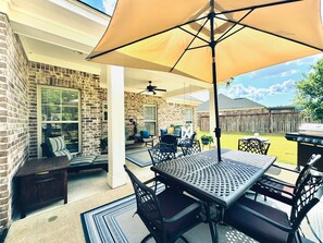 A covered patio area with a table and chairs, a ceiling fan, and a grill in the background.