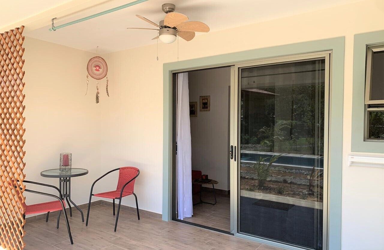 A room with a ceiling fan, a sliding glass door leading to an outdoor area, a small table with two chairs, and a dreamcatcher on the wall.