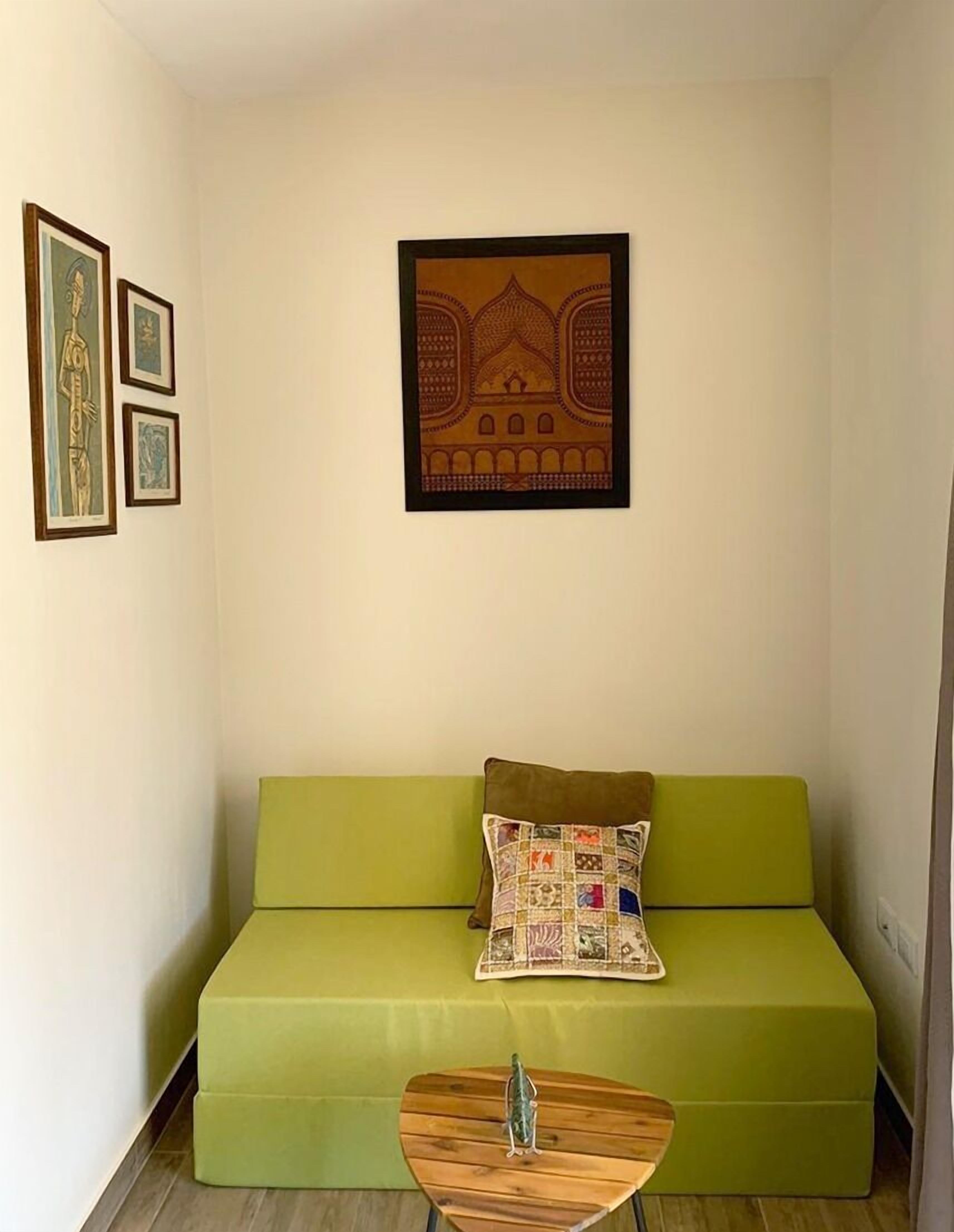 Une pièce avec un canapé vert, une petite table en bois et trois œuvres d’art encadrées accrochées au mur.