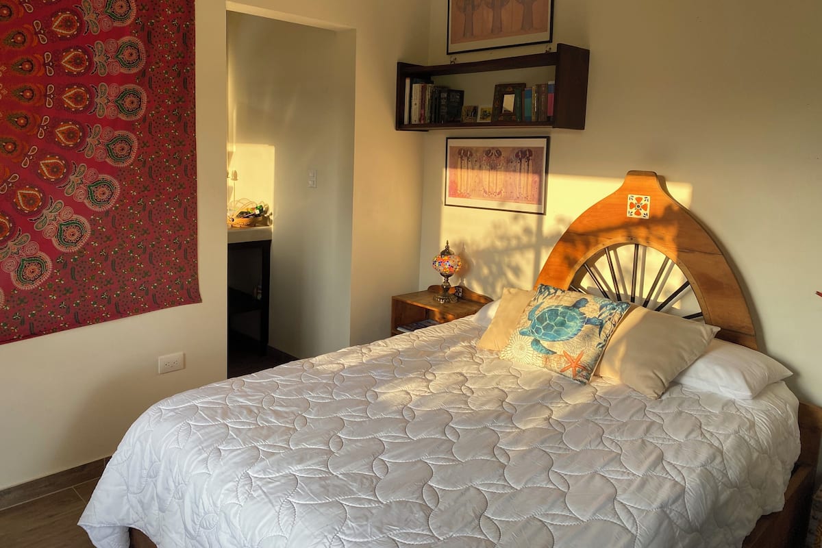 Un dormitorio con cama, cabecera de madera, estantería y un tapiz en la pared.