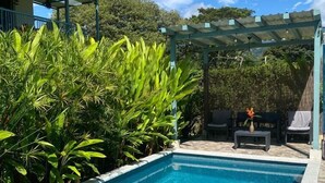A rectangular swimming pool with clear blue water, surrounded by lush green foliage and a pergola structure. - Morning Glory (Bahía Ballena)