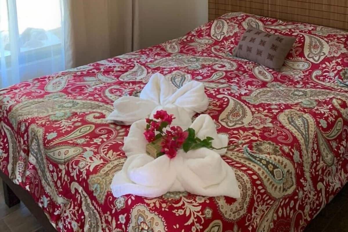 Una habitación de hotel con una cama cubierta con una colcha estampada en rojo y blanco, un cabecero de madera y una lámpara colgante decorativa.