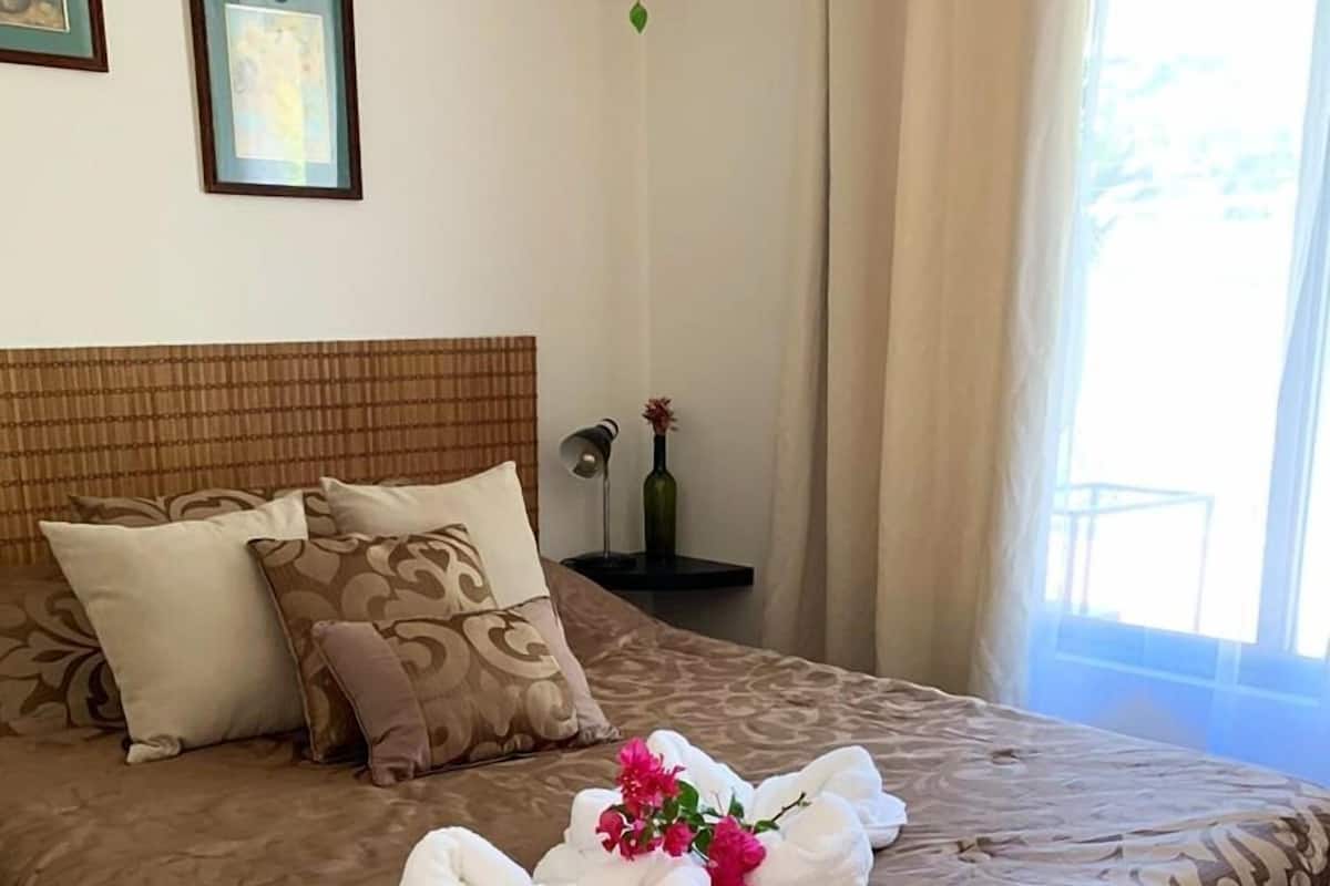 Una cama bien hecha con una colcha marrón estampada, almohadas blancas y un arreglo decorativo de toallas blancas y flores rosas sobre la cama.
