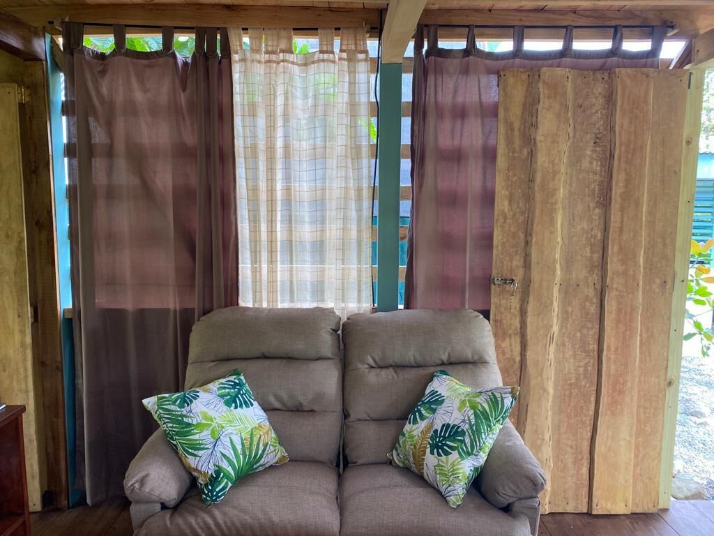 Una habitación con sofá acolchado, dos cojines estampados y un separador de madera.