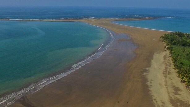 An aerial view of a beach with clear blue waters, a sandy shore, and a small island in the distance. - Morning Glory (Bahía Ballena)