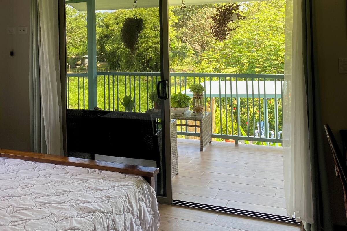 Un dormitorio con cama, puerta corredera de vidrio que da a un balcón con vistas a zonas verdes.