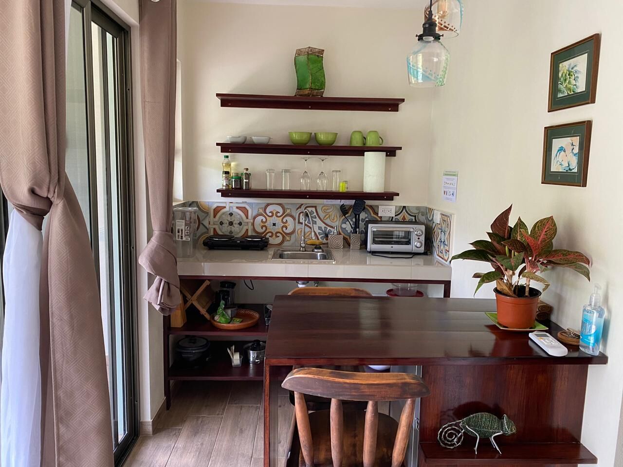 Une cuisine compacte avec des étagères en bois, une table à manger et des chaises. On peut voir une plante en pot sur le comptoir.