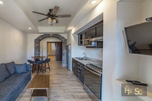 A modern hotel room with a stone archway, a kitchenette, a sofa, and a TV mounted on the wall. - Hotel Suites Cristal Casa Vacacional (San Miguel de Allende)