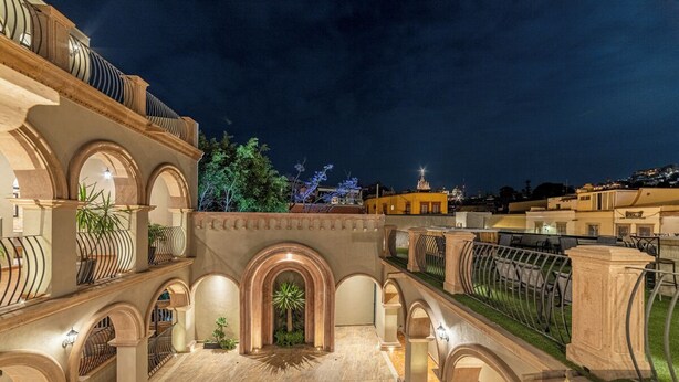 A hotel courtyard with multiple arches, a central fountain, and a view of the city skyline at night. - Hotel Suites Cristal Casa Vacacional (San Miguel de Allende)