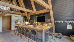 A kitchen with a bar area, wooden beams, and a black wall. - Newly Built Sauna Hot Tub Cold Punge Lazy River Glamp-house by Avantstay (La Pine)