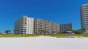 A beachfront hotel with multiple floors, balconies, and a beach in the foreground.