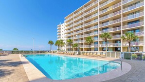 A hotel with a swimming pool, multiple balconies, and palm trees.