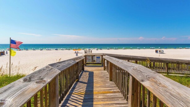 A wooden boardwalk leading to a beach with a flag.