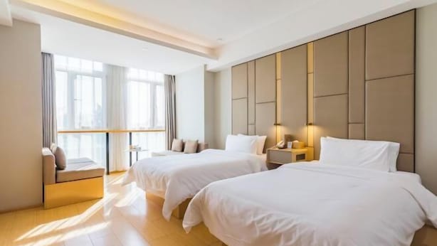 Habitación de hotel con dos camas, un sofá, una mesita de noche y un ventanal con cortinas.