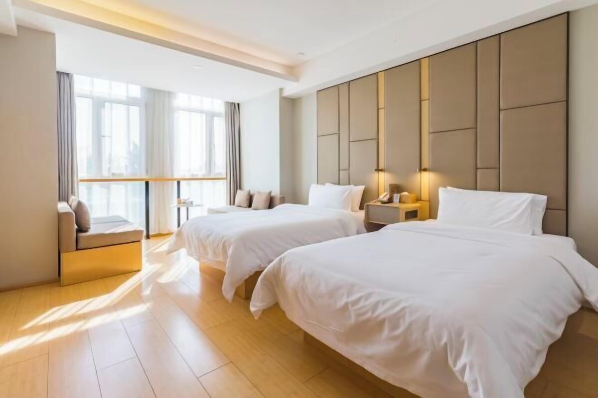 A hotel room with two beds, a sofa, a nightstand, and a large window with curtains.
