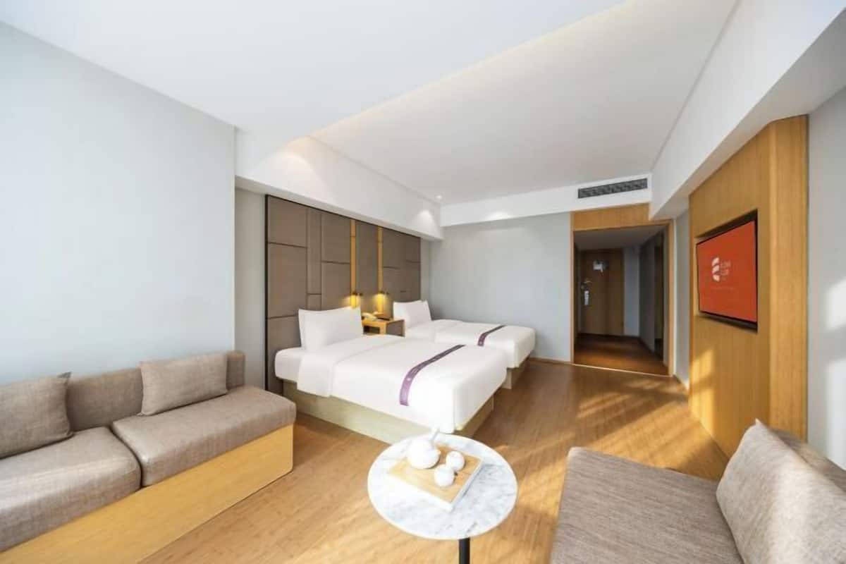 Una habitació d'hotel moderna amb un llit gran, un sofà, una taula rodona petita i un terra de fusta.