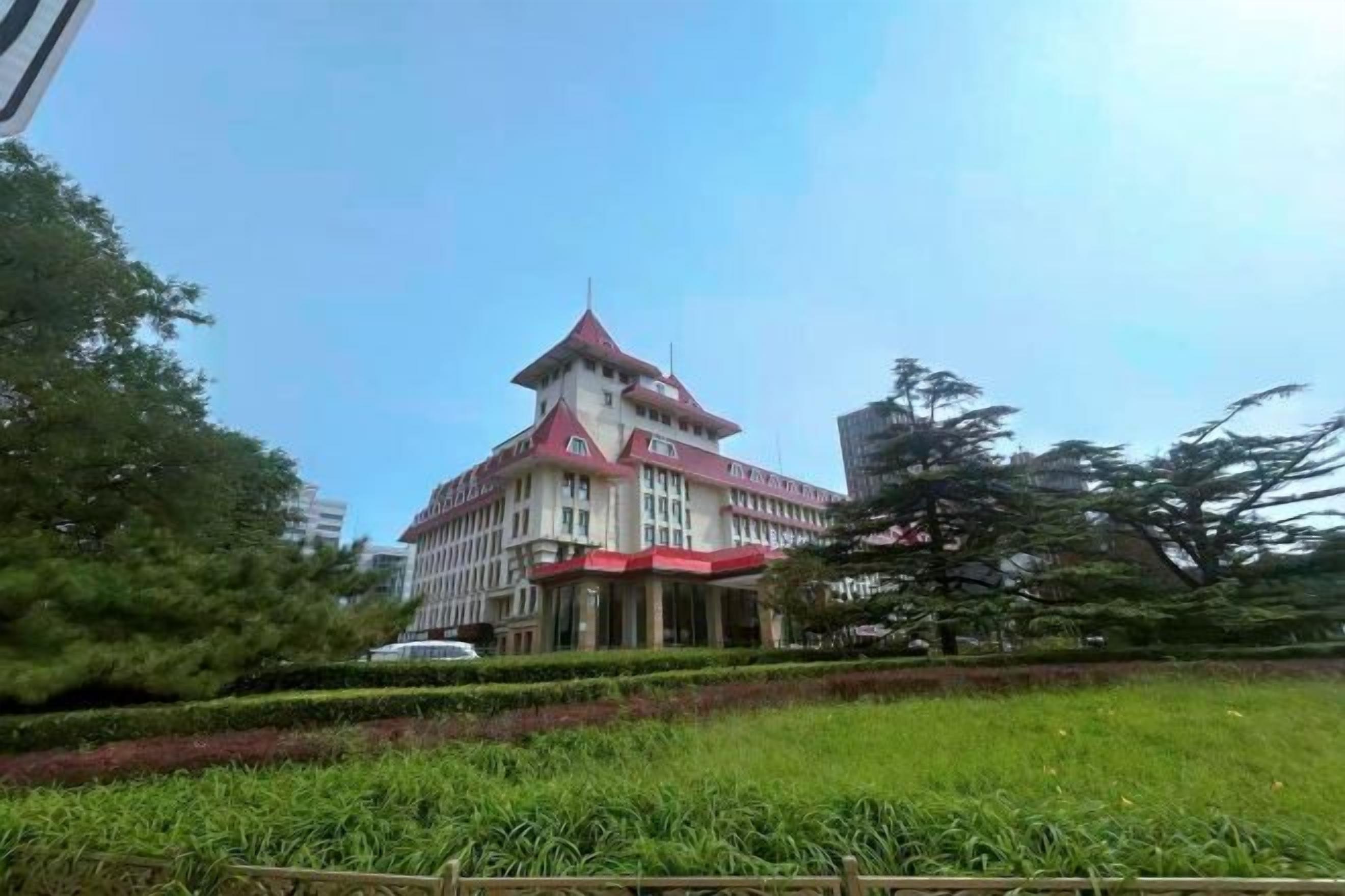 Un edificio de varios pisos con techo rojo y paredes blancas, rodeado de vegetación y árboles.