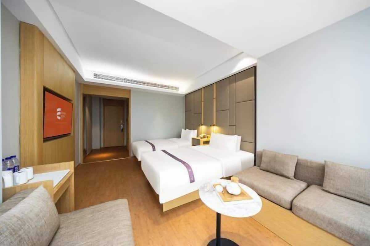 Habitació d'hotel amb dos llits, un sofà, una taula petita amb productes de benvinguda i una televisió penjada a la paret.