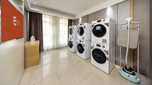Habitación de hotel con área de lavandería que incluye lavadoras apiladas y una lámpara de pie.
