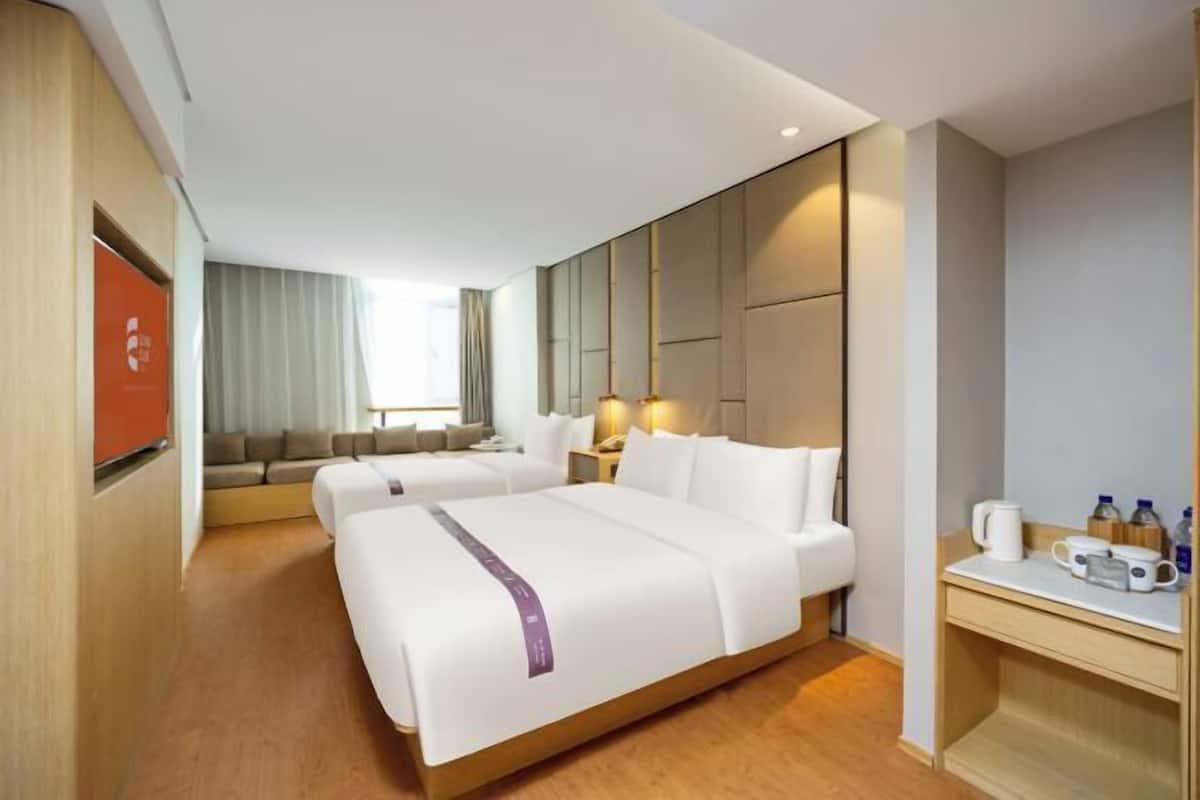 Habitació d'hotel amb dos llits, un sofà, una taula de treball i un escriptori amb una cafetera, i una televisió.