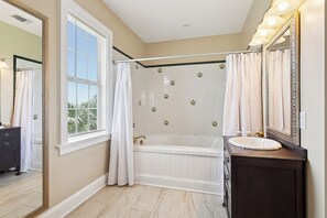 A bathroom with a bathtub, a vanity with a sink, and a large mirror. - Elsa's Place Bed and Breakfast (Lafitte)