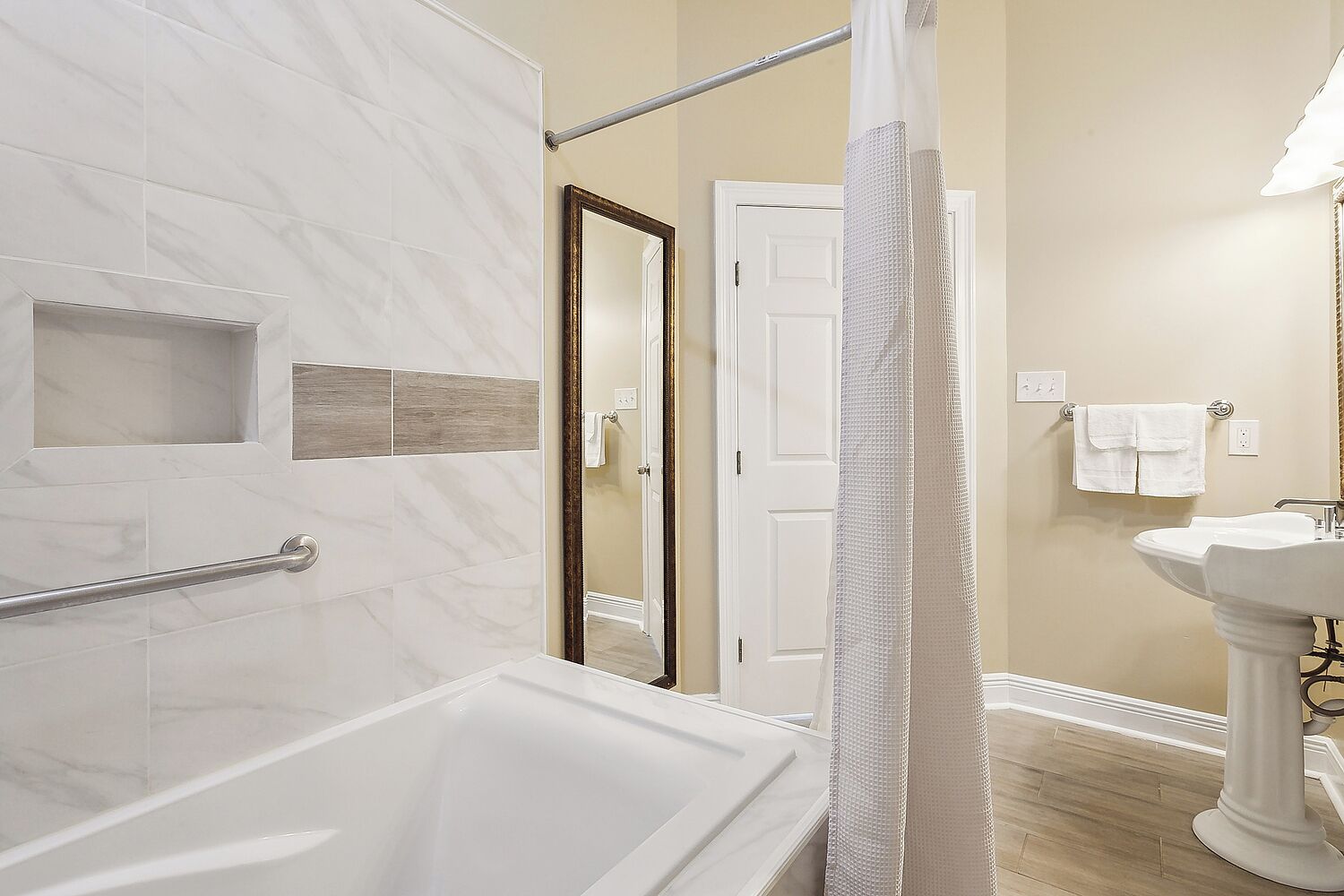 A bathroom with a bathtub, a shower with a curtain, a sink, and a door leading to another room.