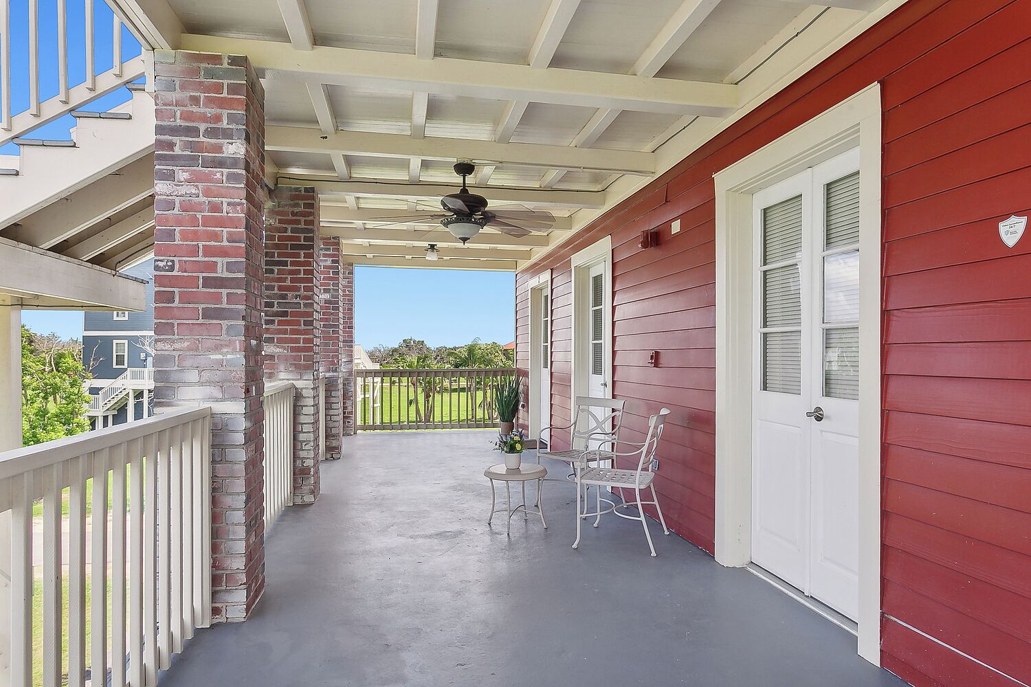 A covered porch with a red exterior, a brick column, a ceiling fan, and two white chairs.