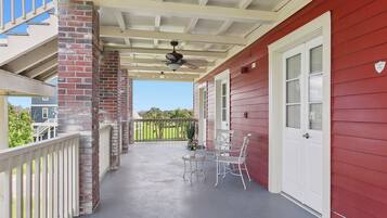 A covered porch with a red exterior, a brick column, a ceiling fan, and two white chairs.