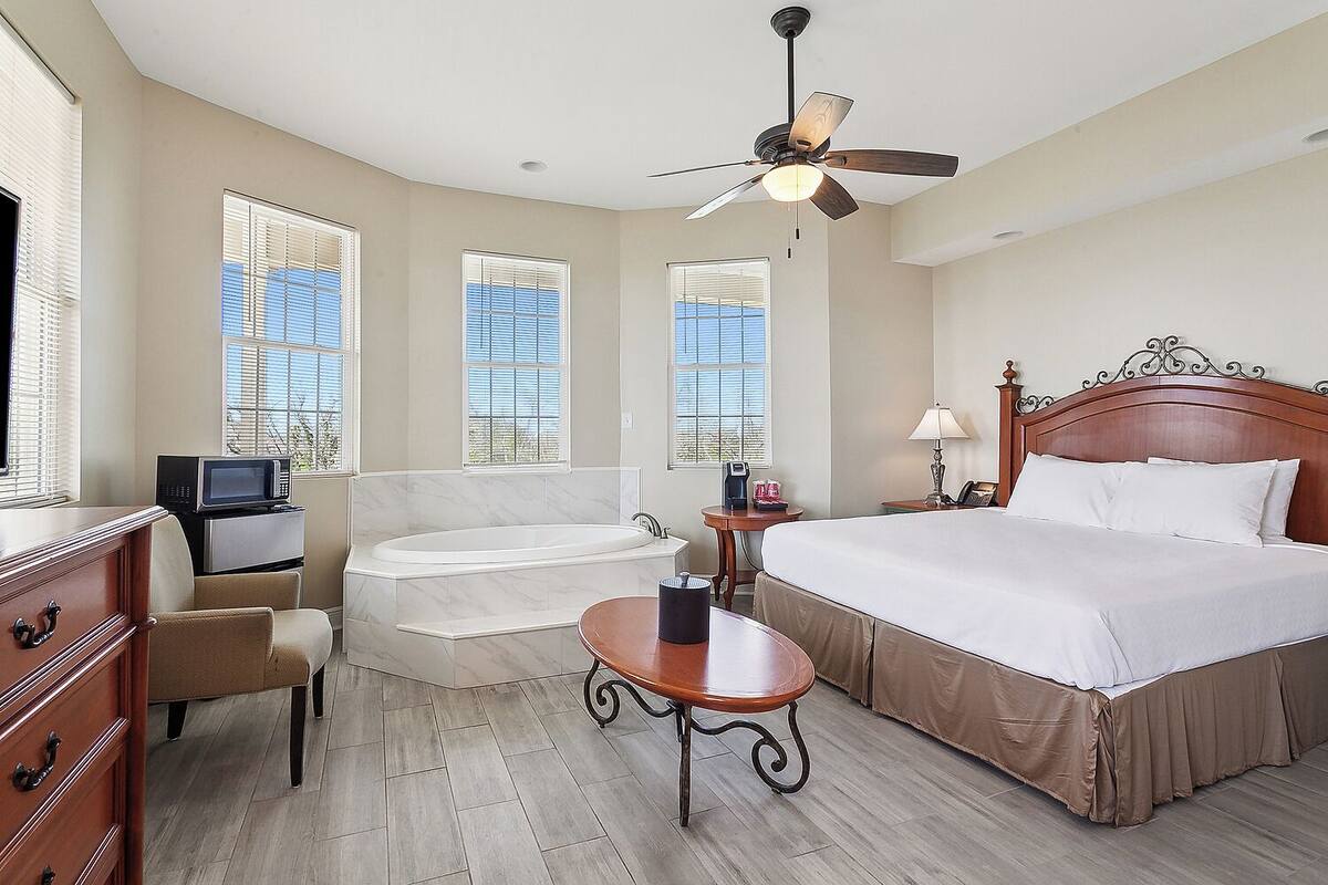 Habitación de hotel con cama, zona de estar con una silla y una mesa, bañera y ventilador de techo.