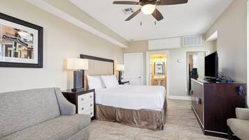 A hotel room with a bed, a desk, a television, and a ceiling fan.