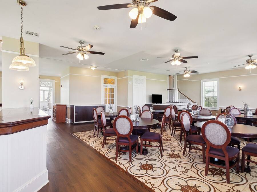 A spacious dining area with multiple round tables and chairs, ceiling fans, and a decorative rug.