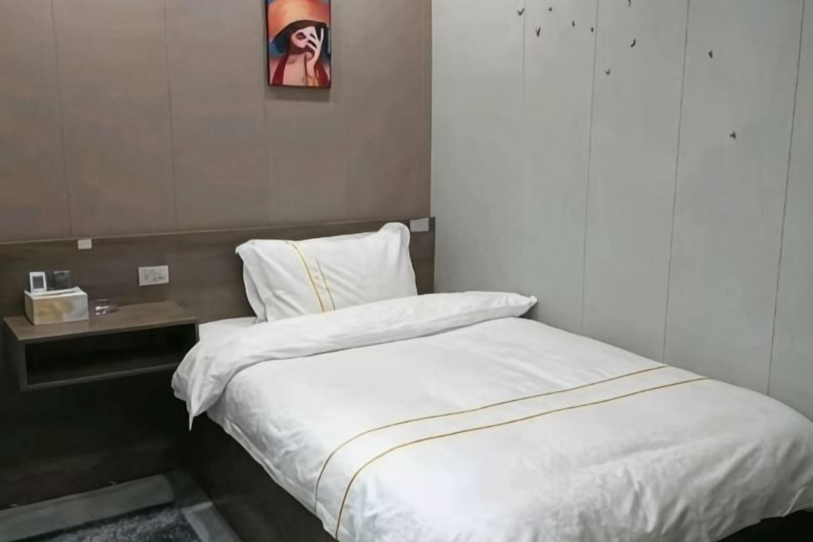 A hotel room with a bed, a nightstand, a wall-mounted shelf, and a painting.