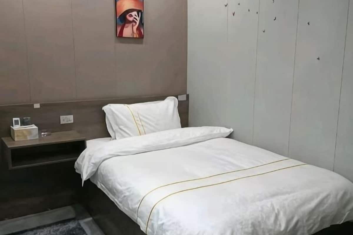 Ένα δωμάτιο ξενοδοχείου με ένα κρεβάτι, ένα κομοδίνο, ένα ράφι τοποθετημένο στον τοίχο και έναν πίνακα.
