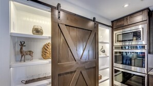 Uma cozinha com porta de celeiro deslizante, eletrodomésticos de aço inoxidável e objetos decorativos nas prateleiras.