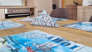 Una stanza con un tavolo da pranzo in legno, tavoli da gioco, una televisione a parete e un angolo cottura con piano cottura e pensili.