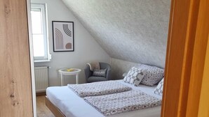 Una camera da letto con soffitto spiovente, un letto con biancheria da letto floreale, un comodino e una sedia con cuscino.
