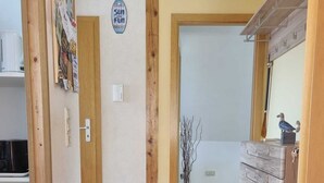 Un corridoio con pavimento in legno, stipite in legno, termostato a muro e una piccola pianta in vaso.