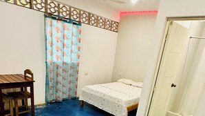 A room with a blue floor, a bed with a white bedspread, a wooden chair, a decorative partition, and a ceiling fan. - Hostal Quistococha  (Laraos)