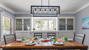 A dining room with a wooden table set for four, white cabinets with glass doors, and a window with blinds.
