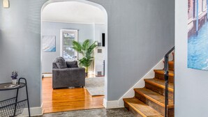 A modern living room with a grey couch, a potted plant, and a staircase leading to another level.
