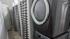 A laundry facility with multiple washing machines and dryers, checkered curtains, and a tiled floor. - Studio with Queen Bed (Robinson)
