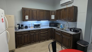 A kitchen with wooden cabinets, a refrigerator, a microwave, a toaster, a sink, and a trash bin. - Studio with Queen Bed (Robinson)