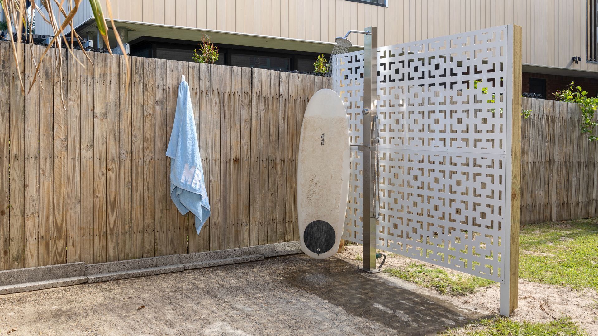 A wooden fence with a towel hanging on it, a white gate, and a concrete ground.