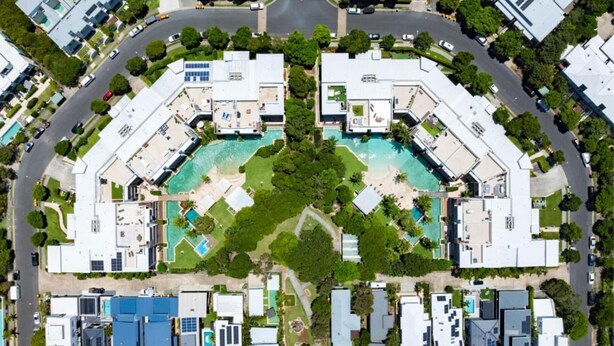An aerial view of a resort with multiple buildings, a central pool, and surrounding greenery. - Drift South 34 - Luxurious rooftop holiday apartment with lagoon pool views (Casuarina)