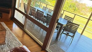 A room with a large sliding glass door leading to an outdoor deck with wooden furniture. - Deckhouse Surfside - Spacious Family Home with Beach Access (Pottsville)