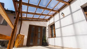 Eine überdachte Terrasse mit Holzbalken, einer Glasabdeckung und einem Blumentopf.