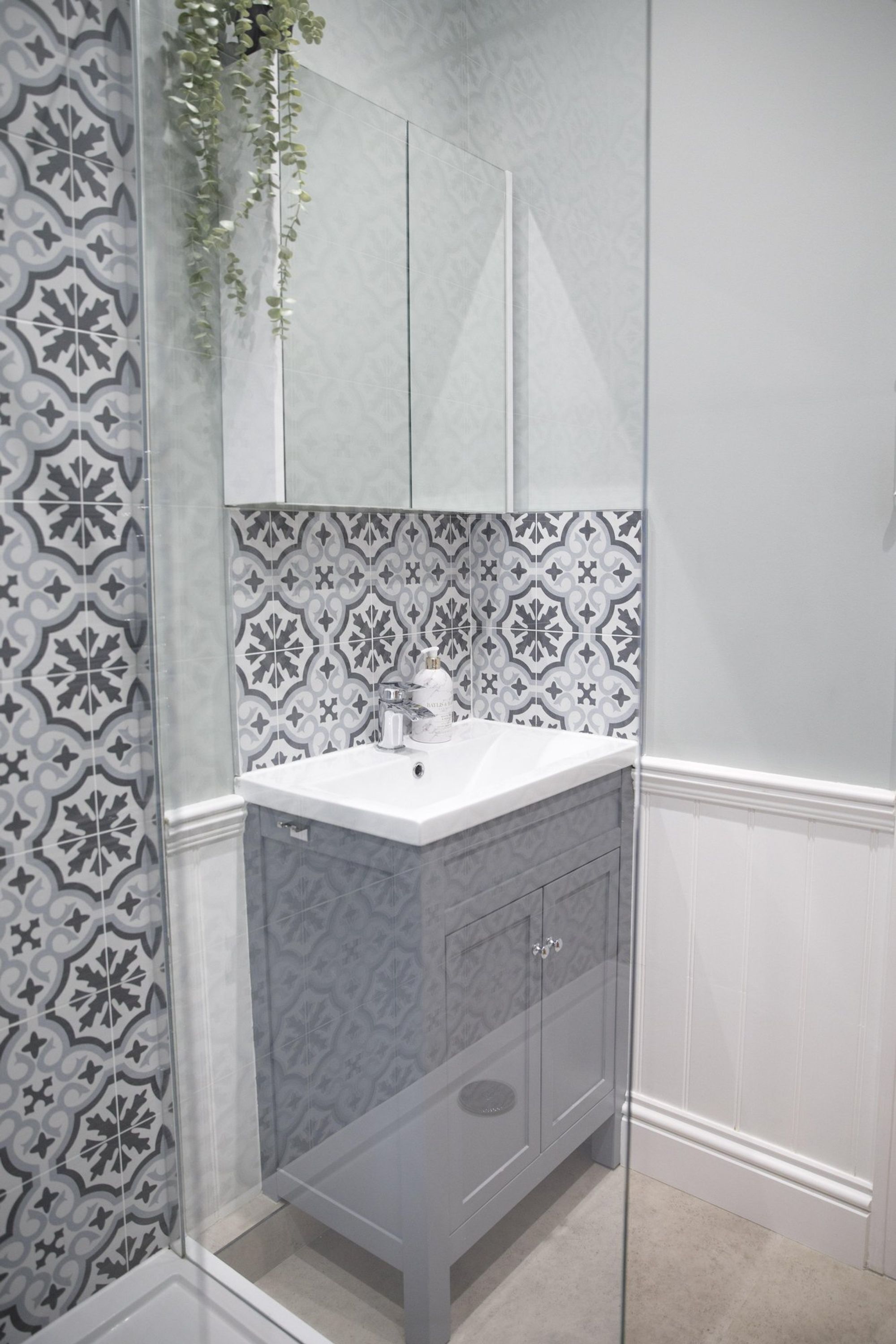 Une salle de bain avec un mur recouvert de carreaux décoratifs, un lavabo blanc et un miroir au-dessus.
