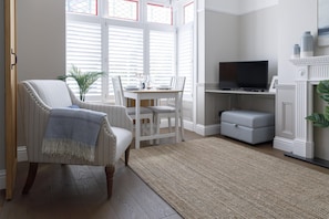 A living room with a white armchair, a dining table with chairs, a flat-screen TV, and a fireplace.