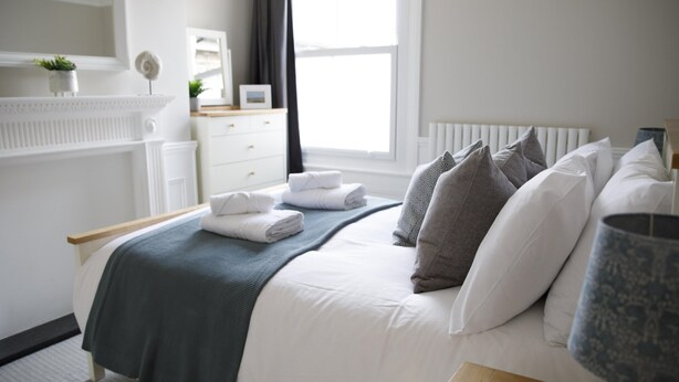 Un lit bien fait, avec une couverture grise, des oreillers blancs et une lampe sur une table de chevet.