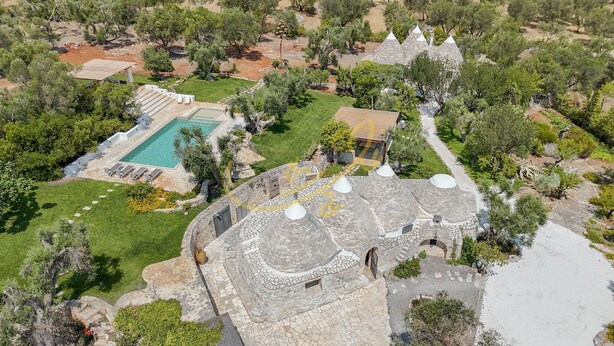 Vista aérea de una propiedad con piscina, arquitectura de piedra y vegetación circundante.